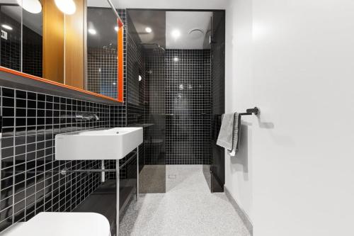 baño de azulejos negros con lavabo y ducha en A Comfy Apt Only a 5-min Walk to Victoria Market, en Melbourne