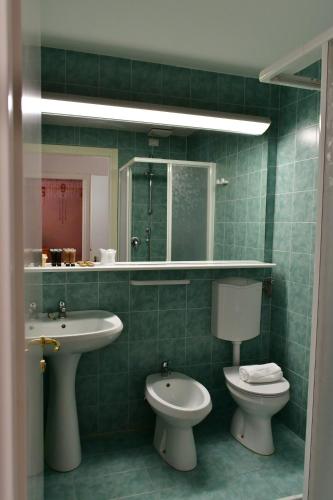 Baño de azulejos verdes con lavabo y aseo en Hotel Saisera, en Valbruna