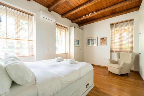 a white bedroom with a large bed and a chair at Athenian 2BR Cottage with Garden & BBQ near Metro in Athens