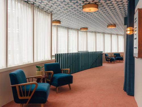 a waiting room with blue chairs and windows at The Hoxton Vienna in Vienna