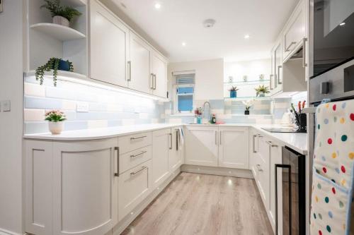a white kitchen with white cabinets and a wooden floor at Luxury 3BRs house in the heart of Victoria in London