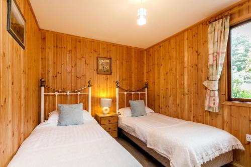 two beds in a room with wooden walls at Yew Tree Lodge in Minehead