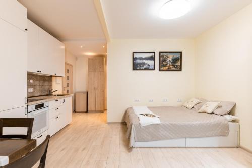 a white bedroom with a bed and a kitchen at Ozo park apartments in Vilnius