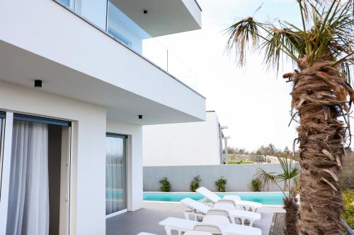 a white house with a palm tree and white lounge chairs at VILLA MARIS SMRIKA in Šmrika