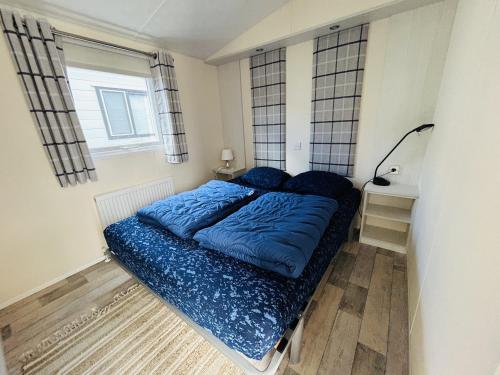 Schlafzimmer mit einem Bett mit blauer Bettwäsche und einem Fenster in der Unterkunft Beach Resort Nieuwvliet-Bad 1240 - EEZZ in Nieuwvliet