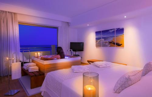 a woman in a bathroom with two beds and a tub at Elysium Resort & Spa in Faliraki