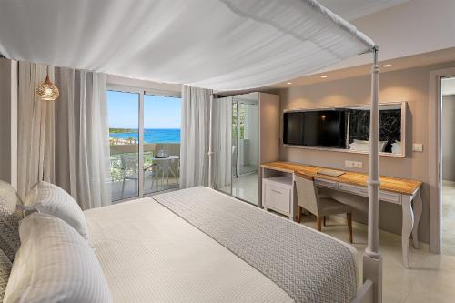 a bedroom with a bed with a desk and a television at Rodos Palladium Leisure & Wellness in Faliraki