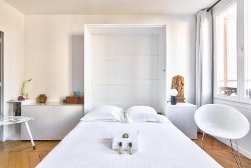 une chambre blanche avec un lit et une chaise dans l'établissement GuestReady - Studio Design près du Moulin Rouge, à Paris
