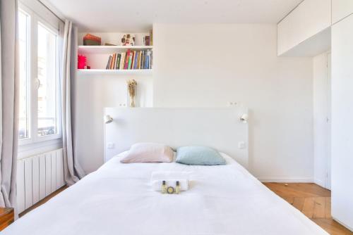 - une chambre blanche avec un grand lit blanc et 2 oreillers dans l'établissement GuestReady - Apt lumineux proche du Moulin Rouge, à Paris