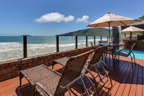a deck with chairs and an umbrella and the ocean at Flat Pietra in Florianópolis