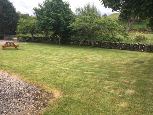 a grassy yard with a picnic table and a stone wall at Ruthven House Holiday Cottages in Kingussie