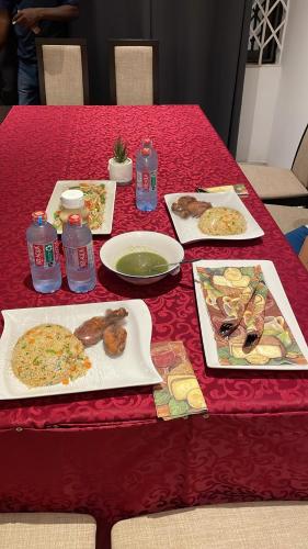 einem roten Tisch mit Teller mit Lebensmitteln und Wasserflaschen in der Unterkunft JLK Guest House & Events Centre in Koforidua