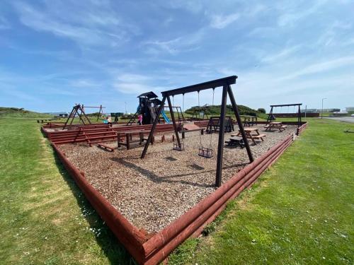 a playground with benches and swings in a field at Burrowhead Holiday Village in Isle of Whithorn