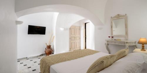 a white bedroom with a bed and a tv at MyBoZer Hotel Kallisto in Imerovigli