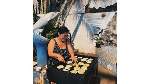 Una mujer está cocinando comida en una parrilla. en Casa Coco Hostel, en Santa Ana