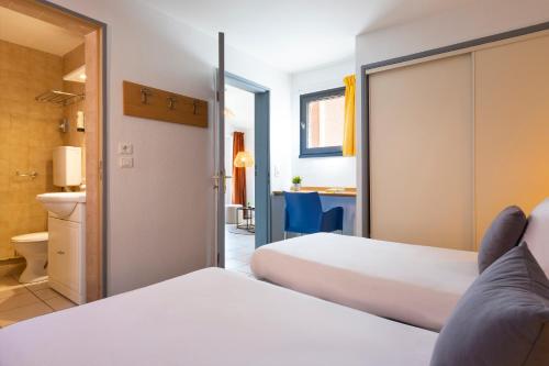 a hotel room with two beds and a bathroom at SOWELL HÔTELS Les Jardins du Cap in Cap d'Agde