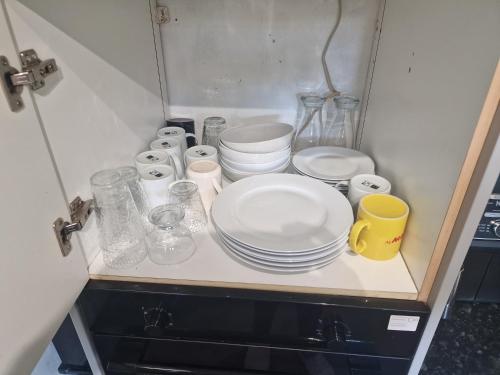 um armário com pratos e óculos e uma caneca amarela em Cozy room Central London - zone 2 - Stockwell em Londres