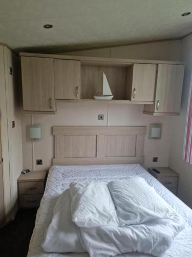 a bedroom with a bed with white sheets and wooden cabinets at Inviting 2-Bed Caravan on Combe Haven Holiday Park in Hollington
