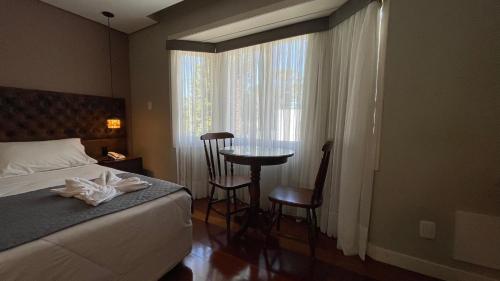 a bedroom with a bed and a table and a window at Pousada Golden Hills in Canela