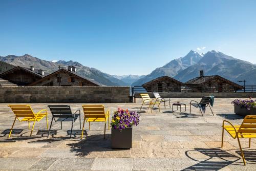 Hôtel Alpen Lodge في لا روزيير: مجموعة من الكراسي والطاولات مع الجبال في الخلفية