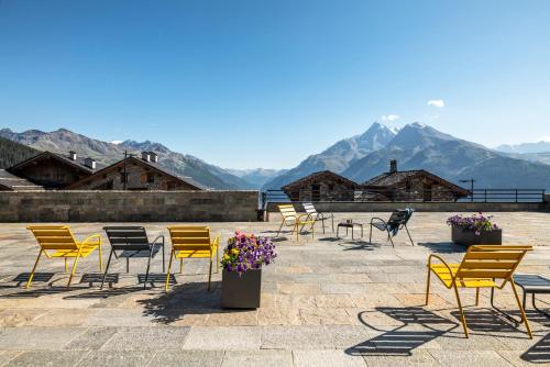 um grupo de cadeiras e mesas com montanhas ao fundo em Residence Alpen Lodge em La Rosière