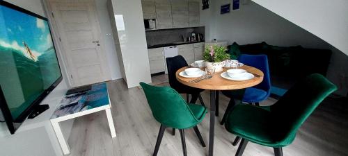 a dining room table with green chairs and a kitchen at Apartament Pogodny in Łeba