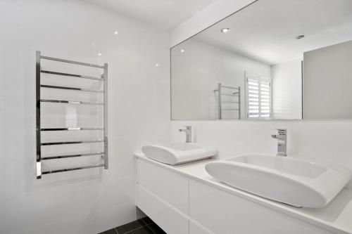 a white bathroom with two sinks and a mirror at Beachfront Dream - Direct Beachfront in Narrabeen