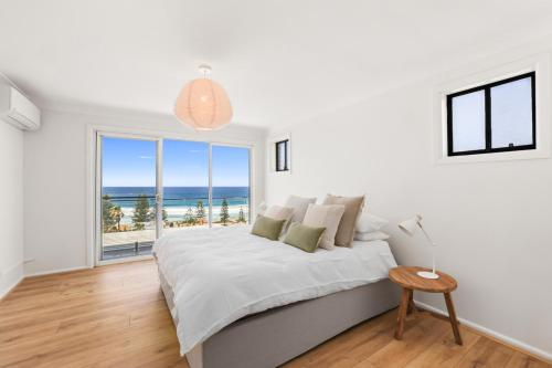 a white bedroom with a bed and a large window at Sweeping Panoramic Views - Brand New Beach House in Curl Curl