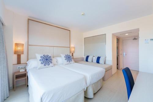 two beds in a hotel room with white and blue pillows at Ferrer Janeiro Hotel & Spa in Can Picafort