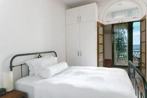 a bedroom with a bed with white sheets and a window at Dungawon - Beachfront in Sydney