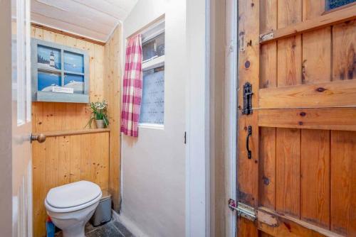 a bathroom with a toilet and a wooden door at Mill Cottage - Cosy & Quaint Cottage - 10 mins from St Andrews in Boarhills