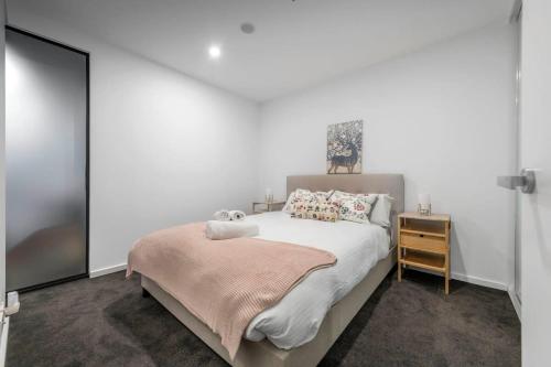 a white bedroom with a bed and a night stand at Park Ave City delight in Canberra