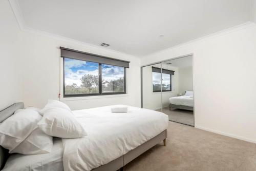 a white bedroom with a large bed and a window at Sensational New Townhouse in Canberra