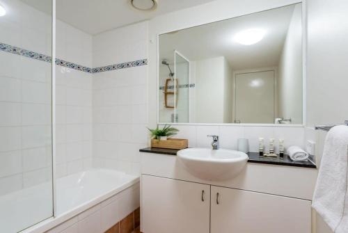 a white bathroom with a sink and a tub and a mirror at Beachfront Oasis with Private Rooftop Retreat in Marcoola