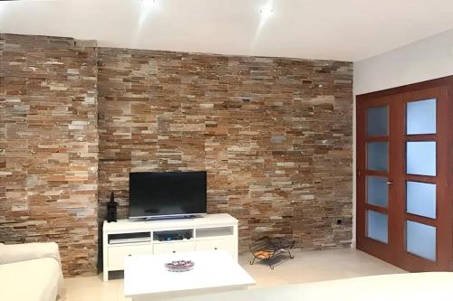 uma sala de estar com uma televisão e uma parede de tijolos em 4 bedrooms villa with private pool furnished terrace and wifi at Calonge em Calonge