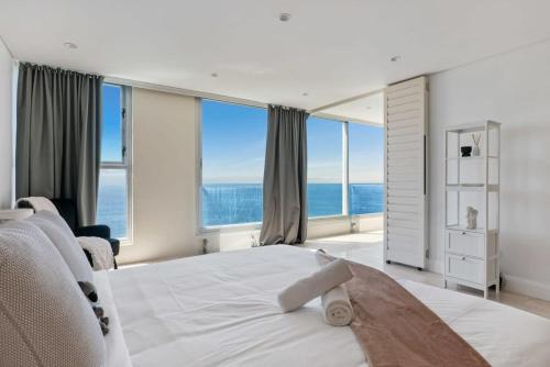 a bedroom with a large white bed with large windows at Clifftop Oasis with Breathtaking Views in Sydney