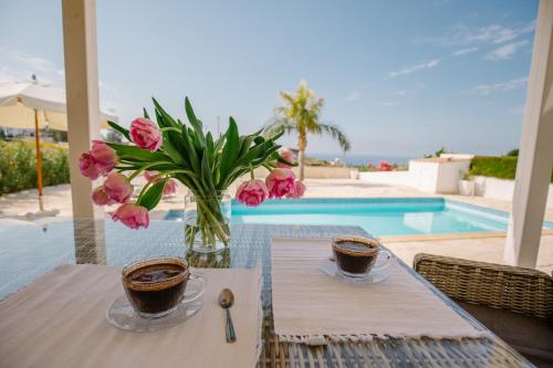 a table with two cups of coffee and pink flowers at Amazing Villa with panoramic sea view in Paphos