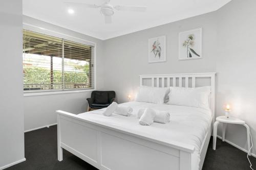 a white bedroom with a large white bed and a window at 'Sanctuary On Walmer' - Sanctuary Point NSW in Sanctuary Point