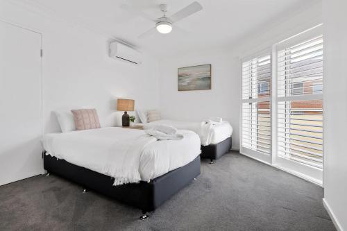 a white bedroom with two beds and a window at Seashells Sweet Retreat - Luxury apartment in Nelson Bay