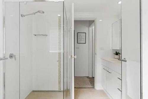 a white bathroom with a shower and a glass door at Beachside Serenity - 100m to Beach in Nelson Bay