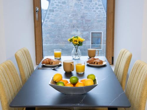 a table with a bowl of fruit and glasses of orange juice at Apartment Harbour Nights 7C by Interhome in Lossiemouth