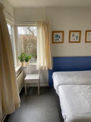 1 dormitorio con 2 camas, silla y ventana en Rustig gelegen bungalow op Texel, en Oosterend
