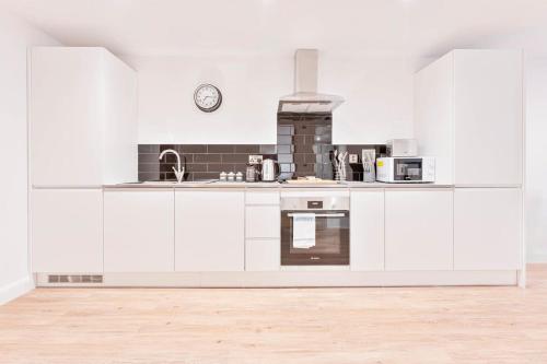 a kitchen with white cabinets and a clock on the wall at Lovely 2 Bed Apartment in Burton-on-Trent in Burton upon Trent