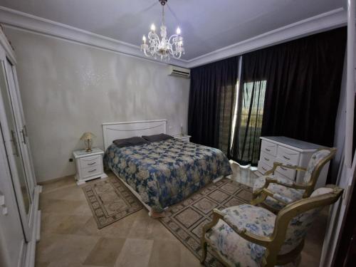 a bedroom with a bed and a chair and a chandelier at Diar Tunis Carthage II in Ariana