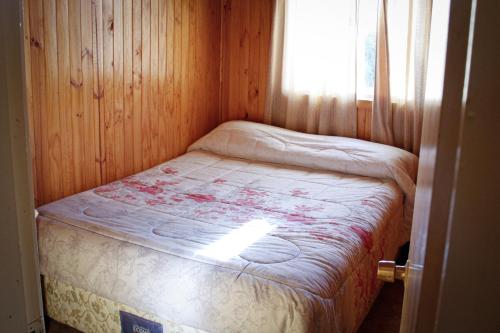a small bed in a wooden room with a window at Cabañas Buenavista Quillón in Quillón