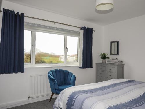 1 dormitorio con cama, silla azul y ventana en Bwthyn Y Bae, en Holyhead