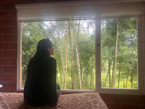 a woman sitting on a bed looking out of a window at Green Bamboo Lodge in San Francisco de Borja
