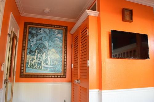 7BD 3BA Parking! 2 min drive to Waikiki Beach! في هونولولو: غرفة بحائط برتقالي مع لوحة وتلفزيون