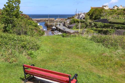 a red bench sitting on a grassy hill overlooking a river at Ty Bara in Cemaes Bay
