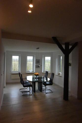 een eetkamer met een tafel, stoelen en ramen bij Großzügige Wohnung auf Resthof in Jevenstedt